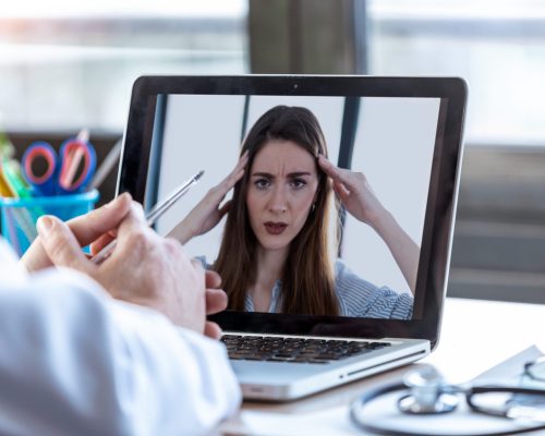 Back view of a doctor attending to a woman patient through a video call with the laptop at home.