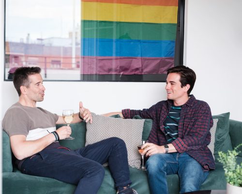 two-young-lgtbi-people-talking-sofa-having-glass-wine-with-lgtbi-pride-flag-hanging-concept-freedom-pride-lifestyle (1)